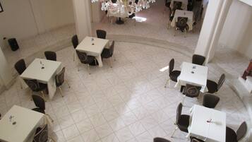 A spacious dining area with multiple tables and chairs, a chandelier, and a tiled floor.