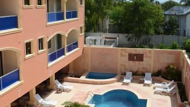 A multi-story building with a swimming pool, lounge chairs, and a water tank on the roof. - Tabarre's Palace (Tabarre)