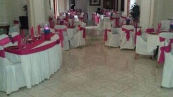 A banquet hall with white tables and chairs, pink sashes, and a tiled floor.