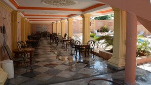 A covered outdoor seating area with tables and chairs, a tiled floor, and a view of a pool and greenery. - Tabarre's Palace (Tabarre)