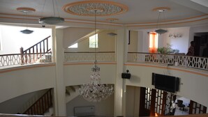 A multi-level interior with a chandelier, a staircase, and a television mounted on the wall. - Tabarre's Palace (Tabarre)