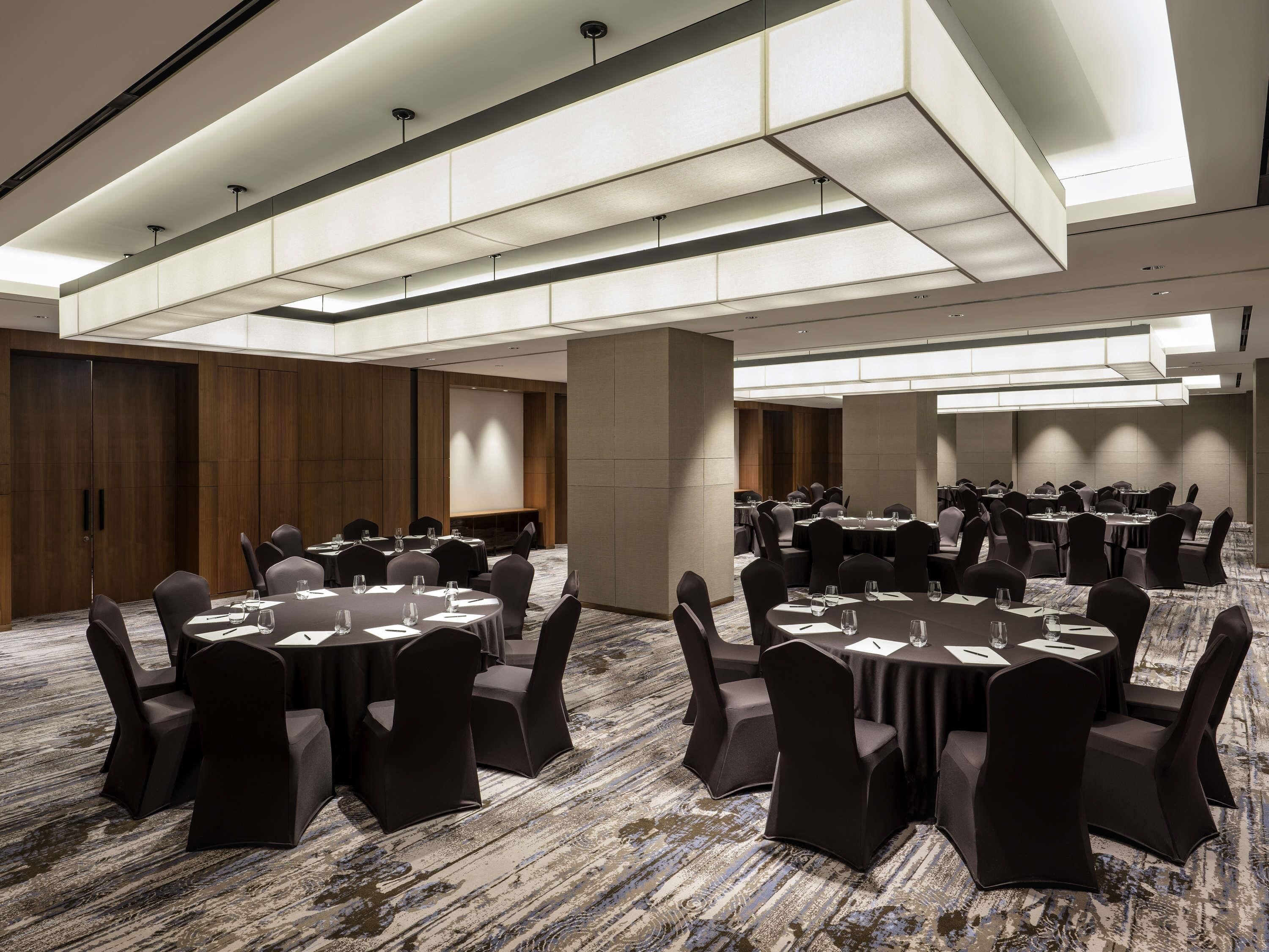 Un salón de conferencias con mesas redondas, sillas negras y una pantalla grande.