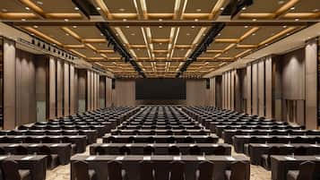 A conference room with rows of tables and chairs, a large screen at the front, and a modern ceiling design.