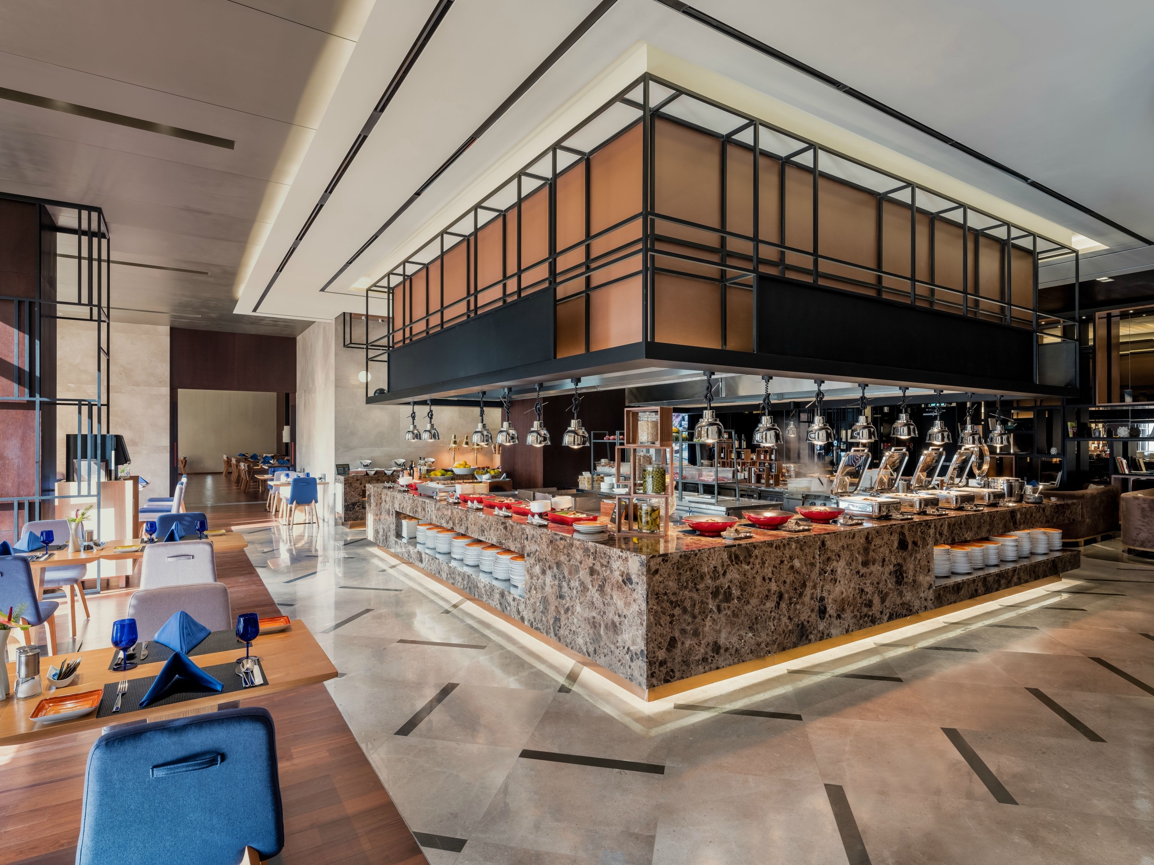 Un hall d’hôtel moderne doté d’un bar central, de différents espaces aménagés pour s’asseoir et d’une disposition spacieuse.