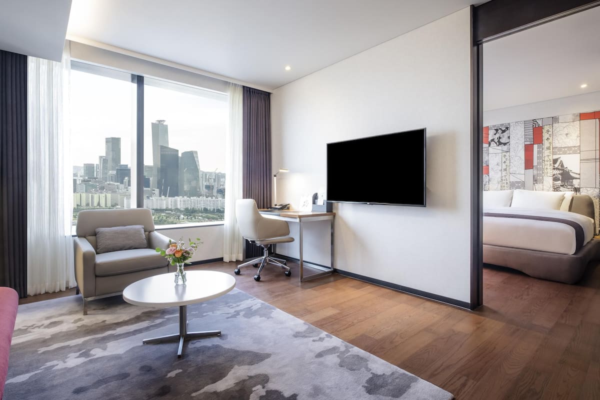 Et moderne hotelværelse med byudsigt, et fladskærms-tv, et skrivebord, en sofa og en seng.
