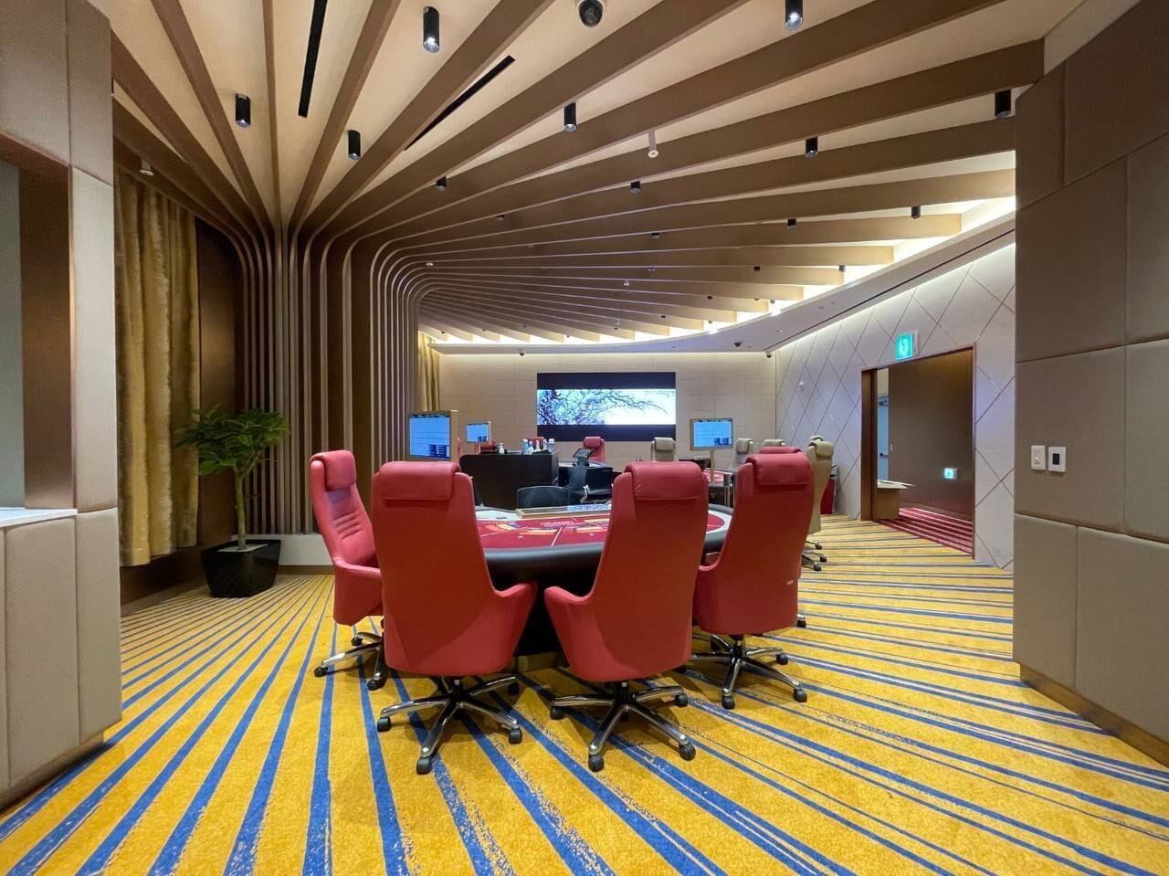 A conference room with a long table, red chairs, and a large screen at the front.