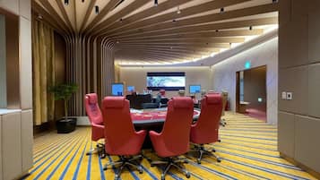 A conference room with a long table, red chairs, and a large screen at the front.