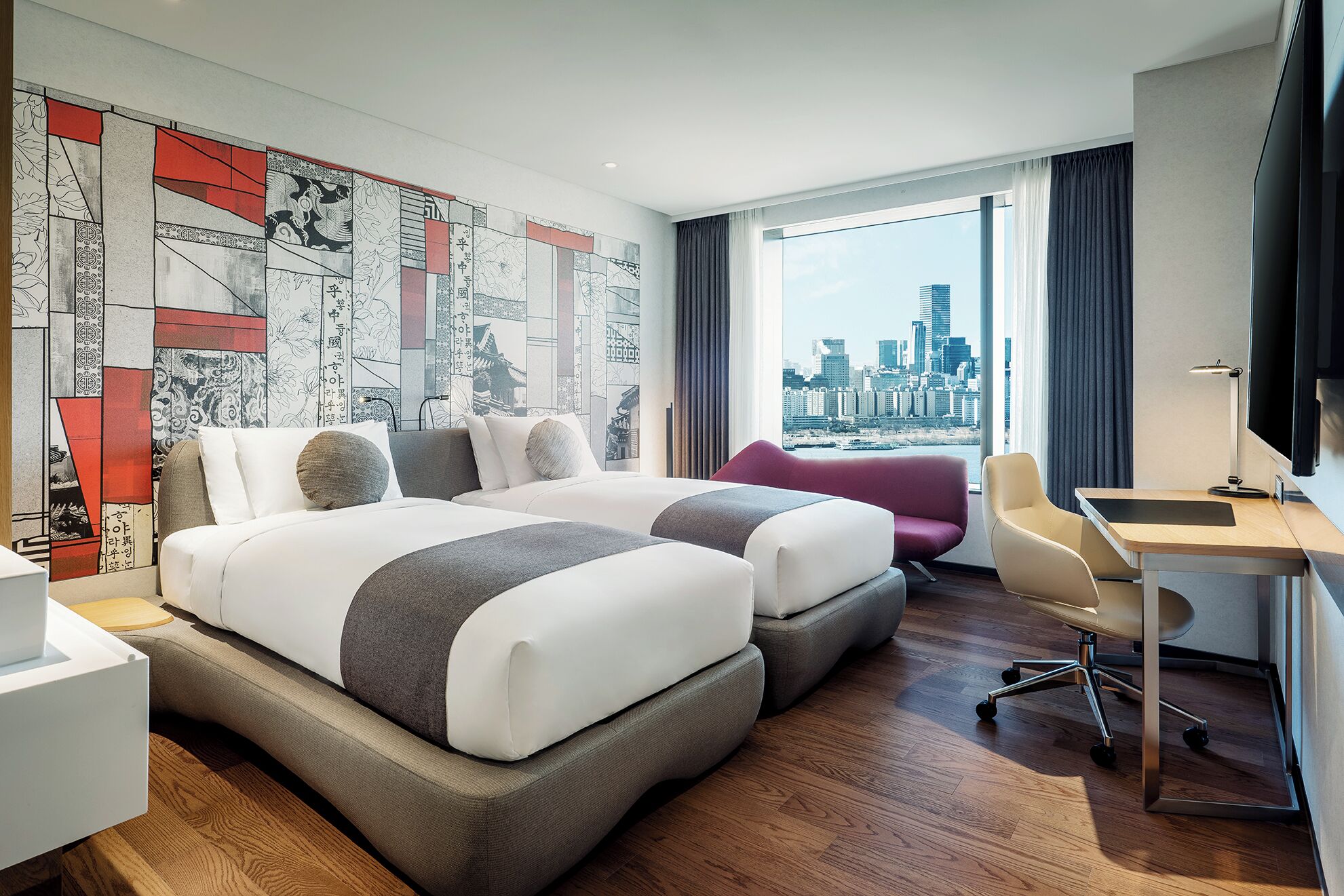 A modern hotel room with a large bed, a desk, and a view of the city skyline.