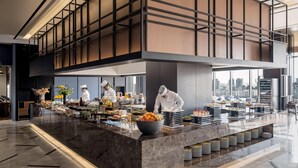 A modern kitchen with chefs preparing food, a buffet setup, and a city view through large windows. - Novotel Ambassador Seoul Yongsan - Seoul Dragon City (Seoul)