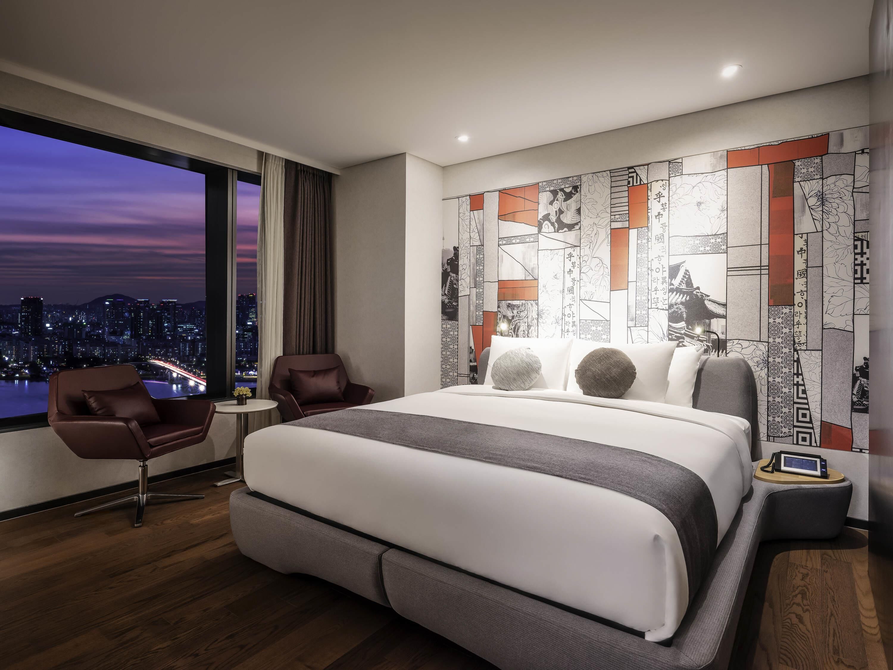 Una habitación de hotel moderna con una cama grande, una zona de estar y vistas a la ciudad.