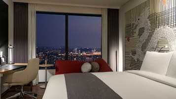 Habitación de hotel moderna con una cama grande, un escritorio y vista a la ciudad de noche.