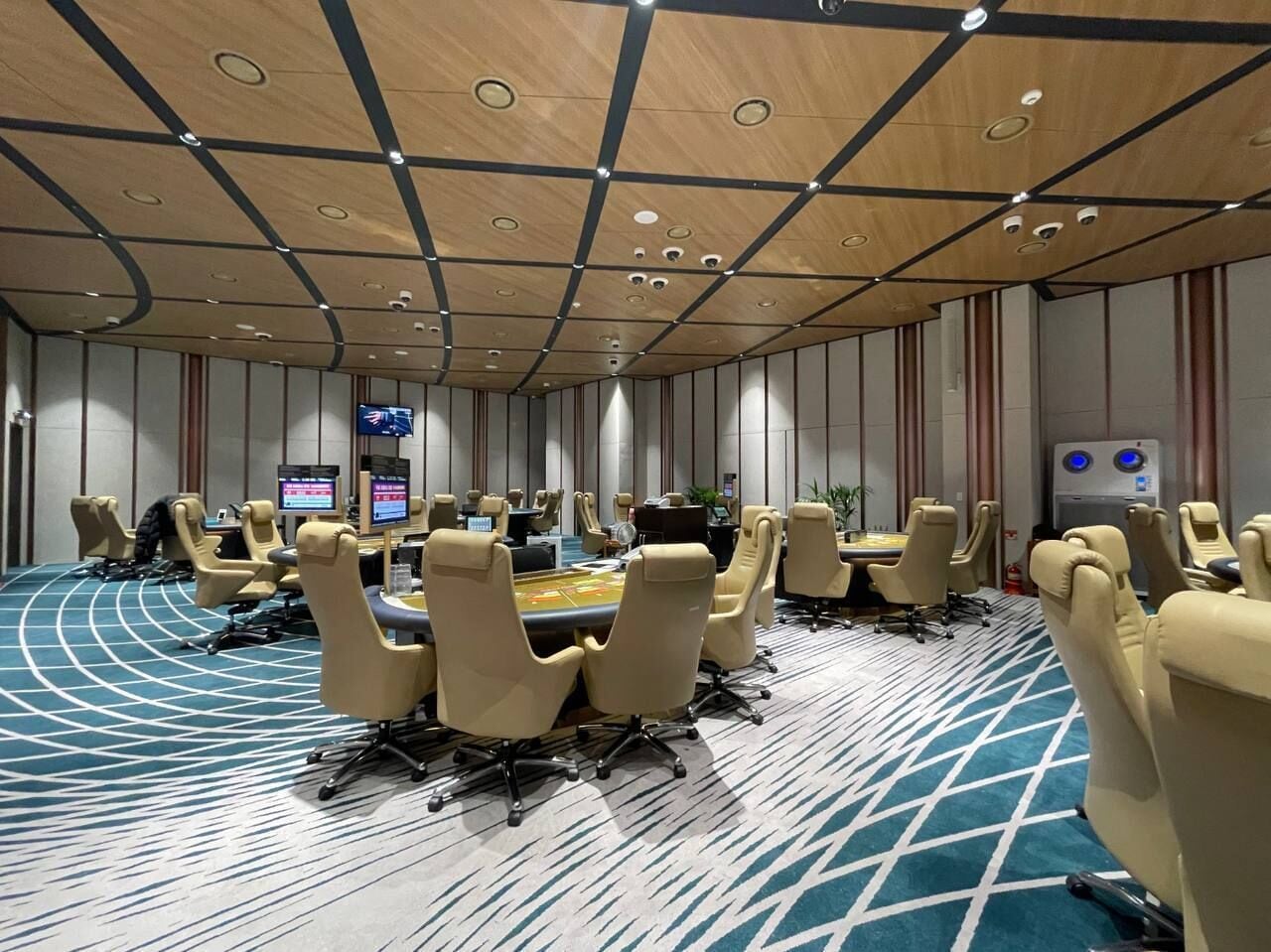 Un salón de conferencias con una amplia mesa ovalada rodeada de sillas color beige, suelo alfombrado y techo de madera con iluminación empotrada.
