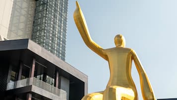 Una estatua dorada de una figura humana con los brazos extendidos, ubicada frente a un edificio moderno con fachada de vidrio y un balcón.