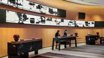 A modern reception area with a curved wooden wall, a large black and white artwork, and a reception desk with two staff members.