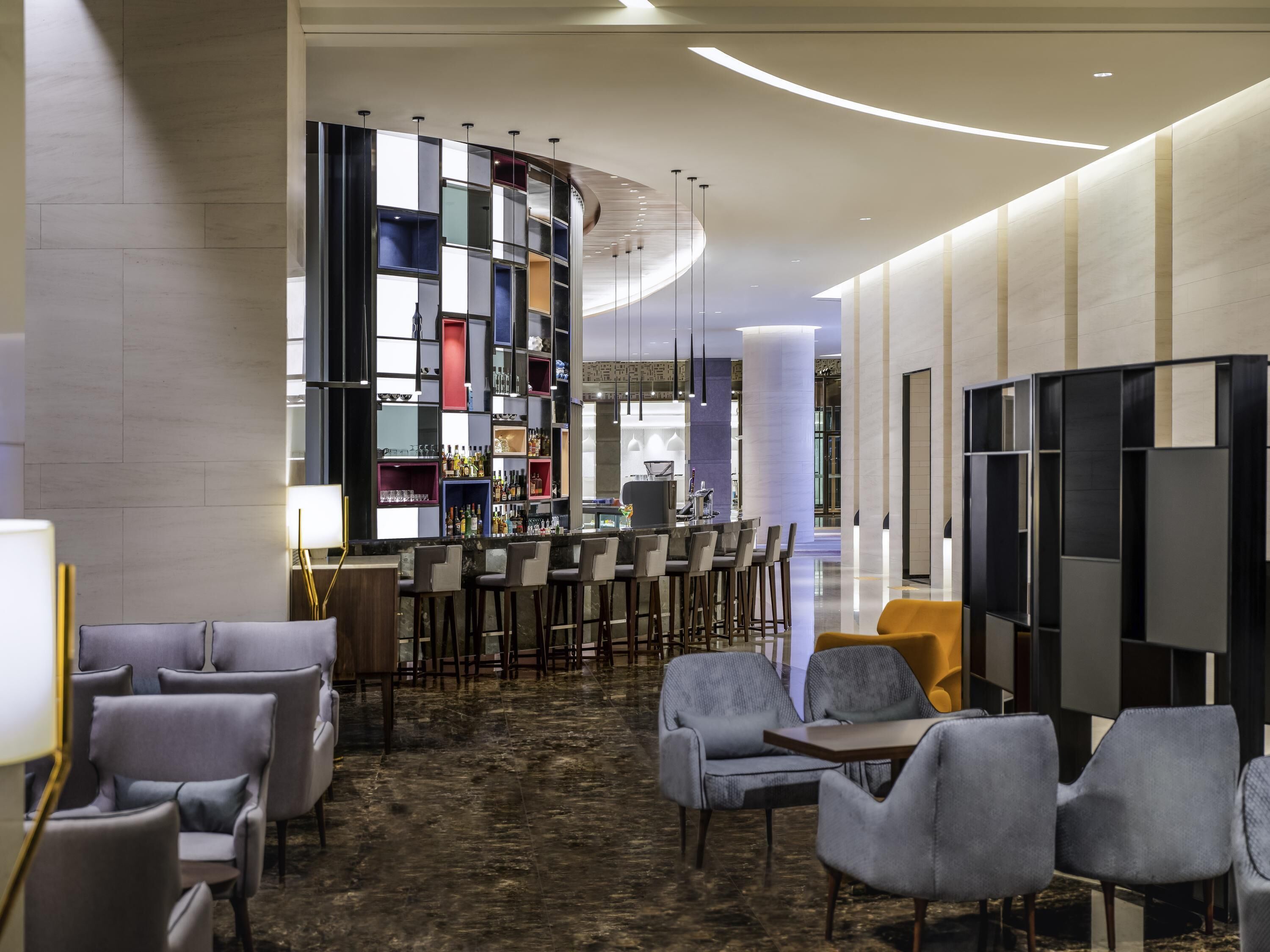 En moderne hotellobby med barområde, siddepladser og en dekorativ væg med reoler.