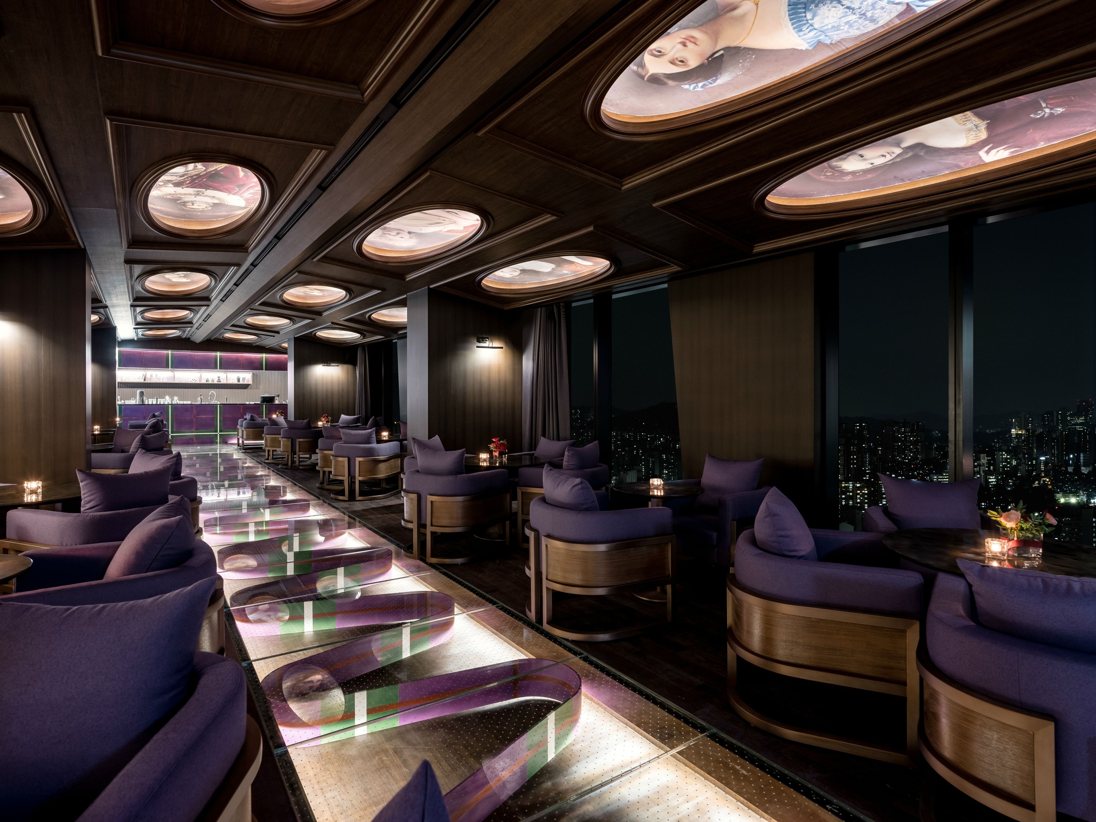 Un salón moderno con una barra alargada, asientos cómodos y amplios ventanales con vistas a la ciudad.