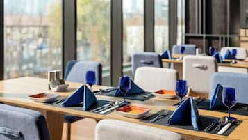 A modern dining area with tables set for two, featuring blue napkins and wine glasses.