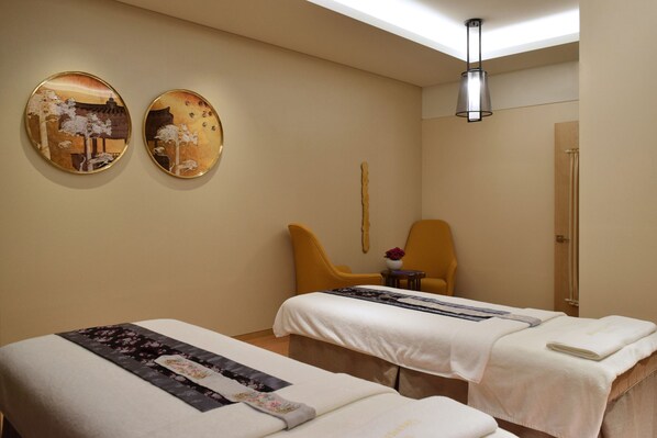A hotel room with two beds, a sitting area with a chair, a small table with a vase, and two wall-mounted mirrors.
