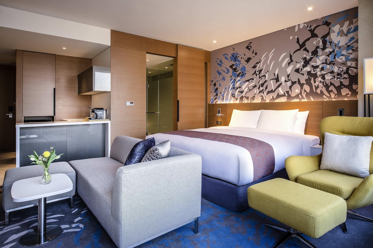 Une chambre d’hôtel moderne équipée d’un lit, d’un canapé, d’une petite table avec un vase et d’une kitchenette.