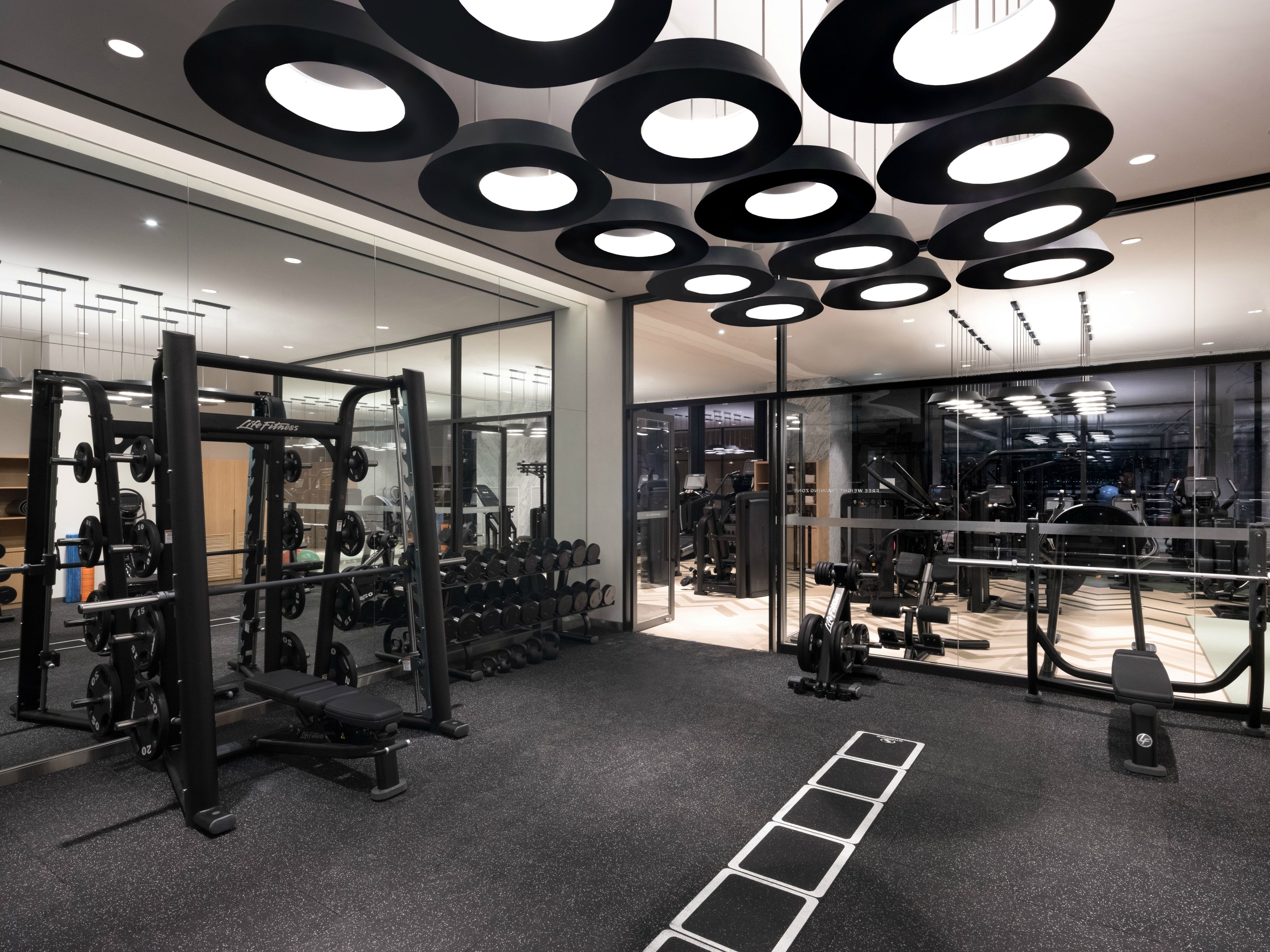 A modern gym with mirrored walls, various exercise equipment, and a black and white color scheme.