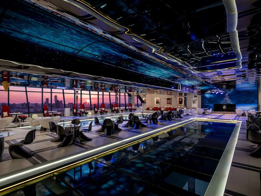 A modern conference room with a city view, glass tables, and red chairs.