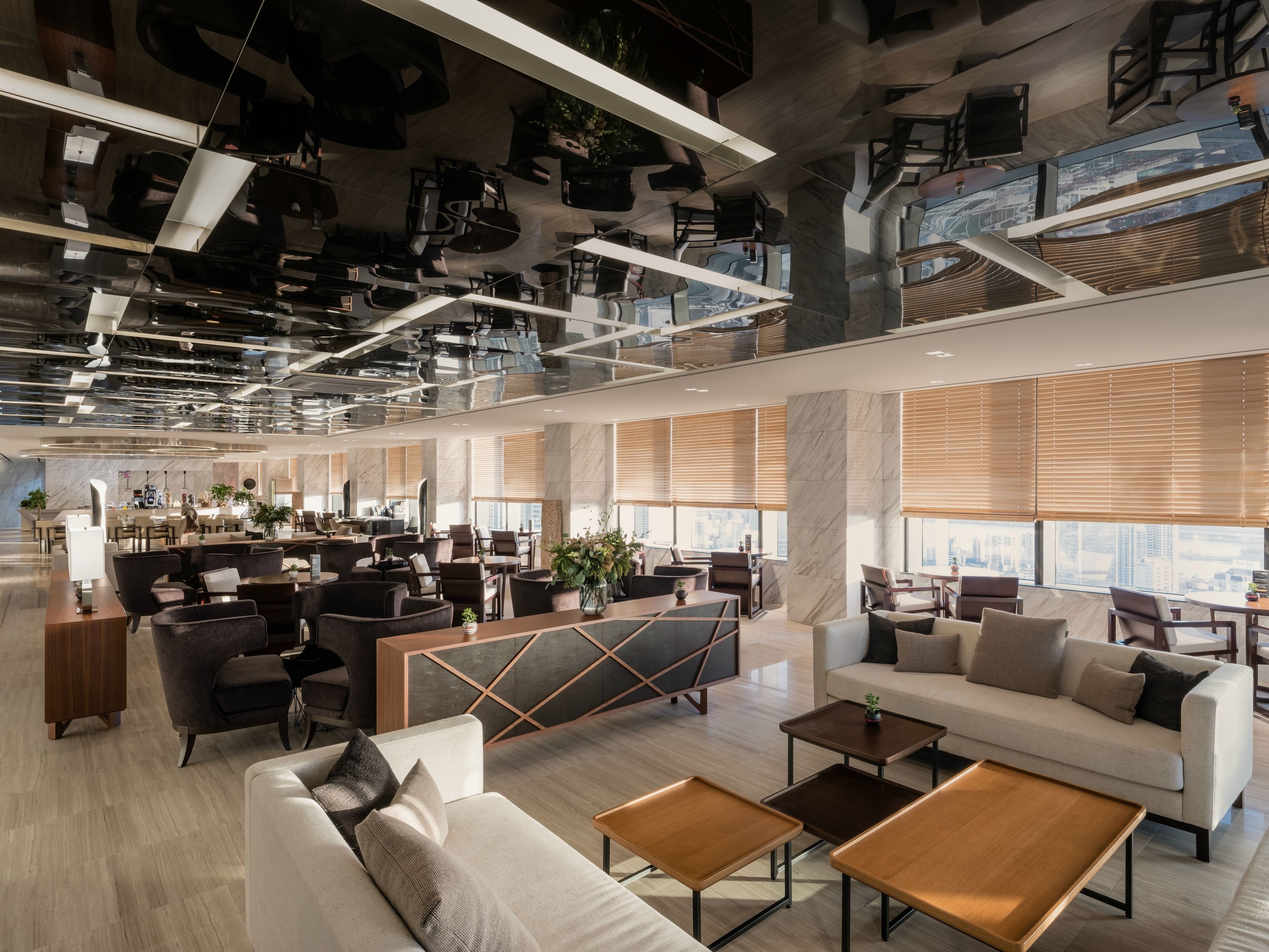 A spacious hotel lobby with modern furnishings, large windows, and a high ceiling with unique lighting fixtures.