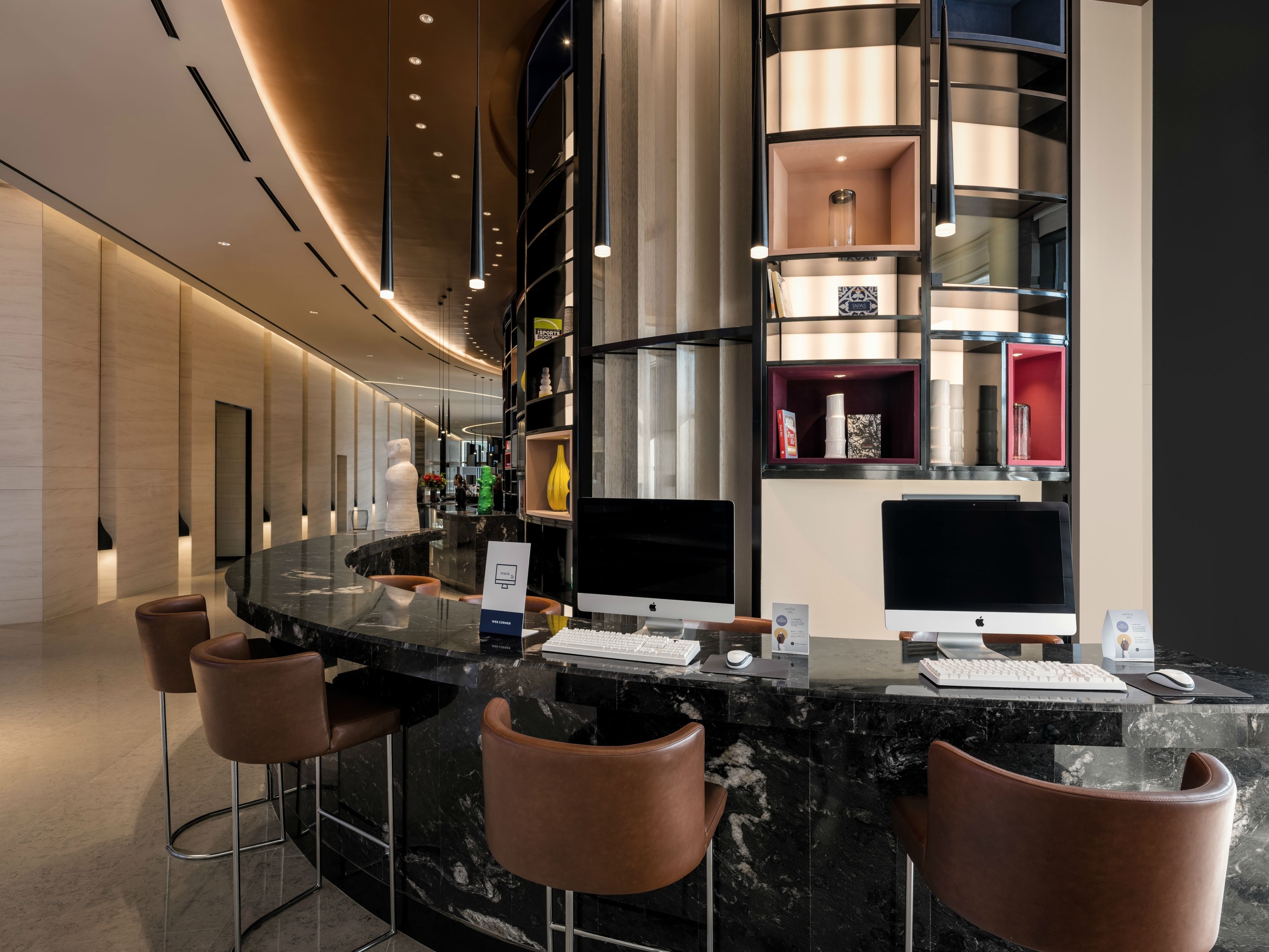 A modern bar area with marble countertops, leather bar stools, and multiple Apple iMac computers.