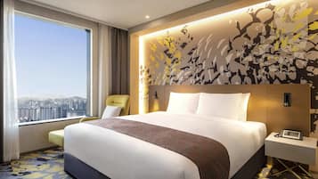 Habitación de hotel moderna con una cama grande, vista a la ciudad, un muro decorativo y un pequeño escritorio con teléfono.
