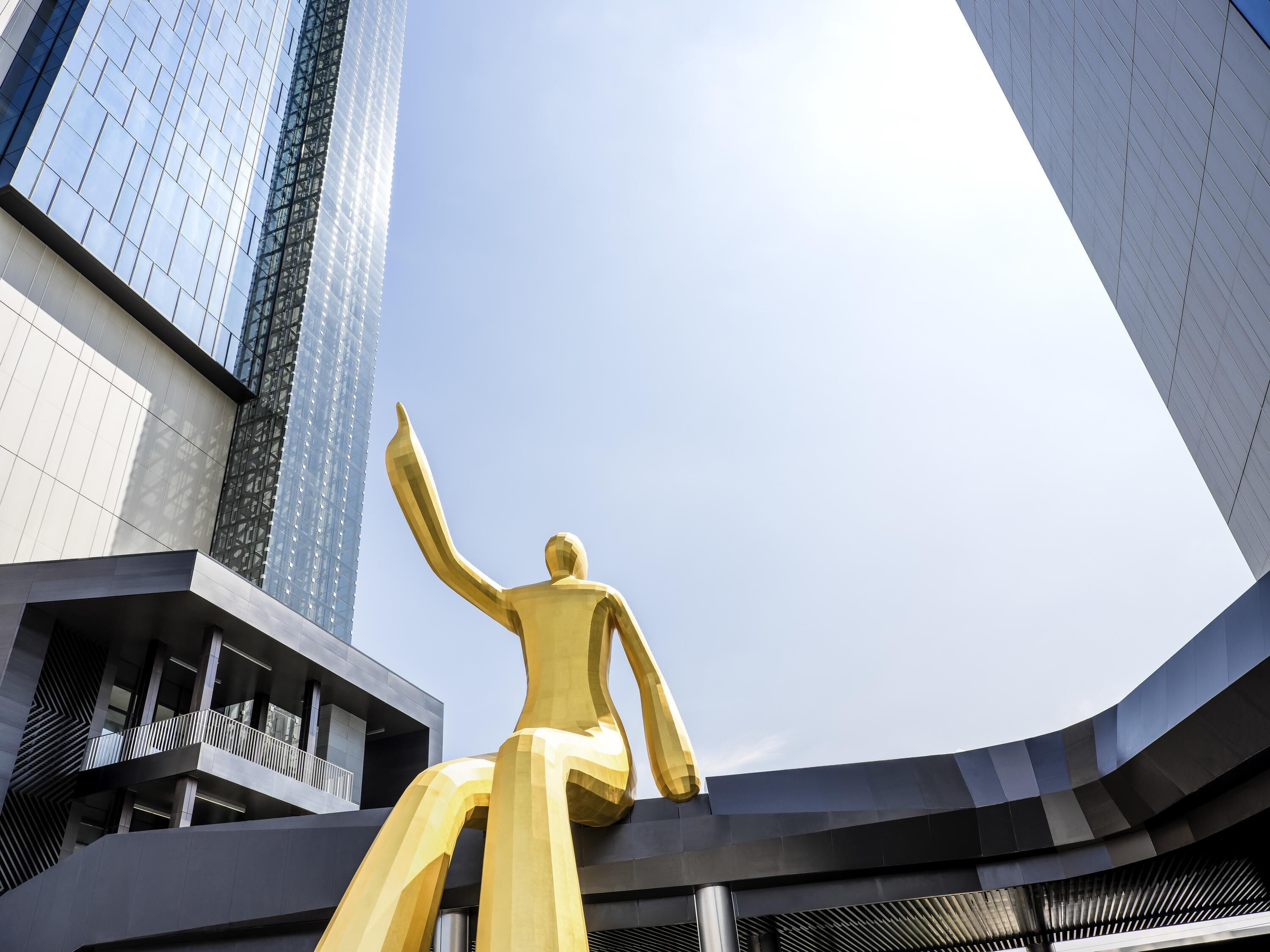 A golden statue in an urban setting with modern buildings in the background.