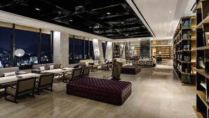 A modern interior with a seating area, a large window with a city view, and a bookshelf. - Novotel Suites Ambassador Seoul Yongsan - Seoul Dragon City (Seoul)