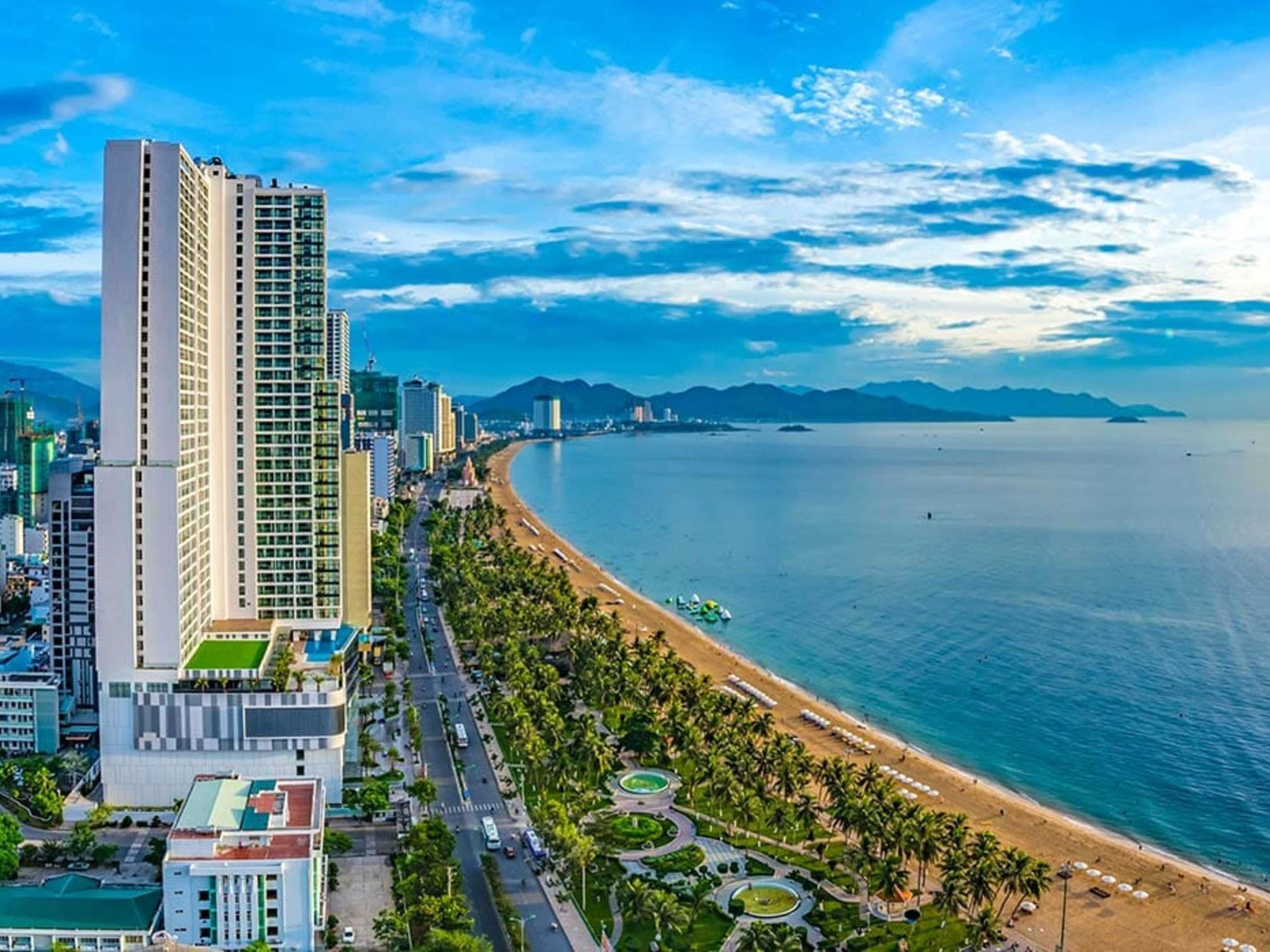 A coastal cityscape with a prominent high-rise hotel, a beach, and a clear view of the sea.