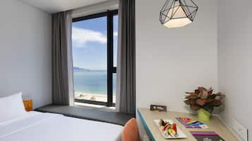 Habitación de hotel con una cama, un escritorio con una planta y vista al océano.