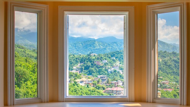 Habitació amb tres finestres que donen vistes a un paisatge montanyós amb edificis dispersos.