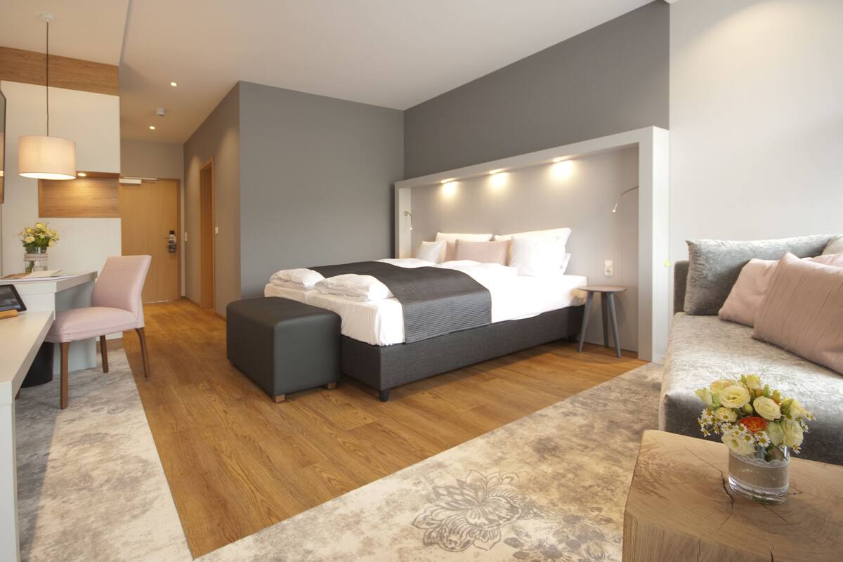 A modern bedroom with a bed, bedside tables, a desk, a chair, and a sofa.