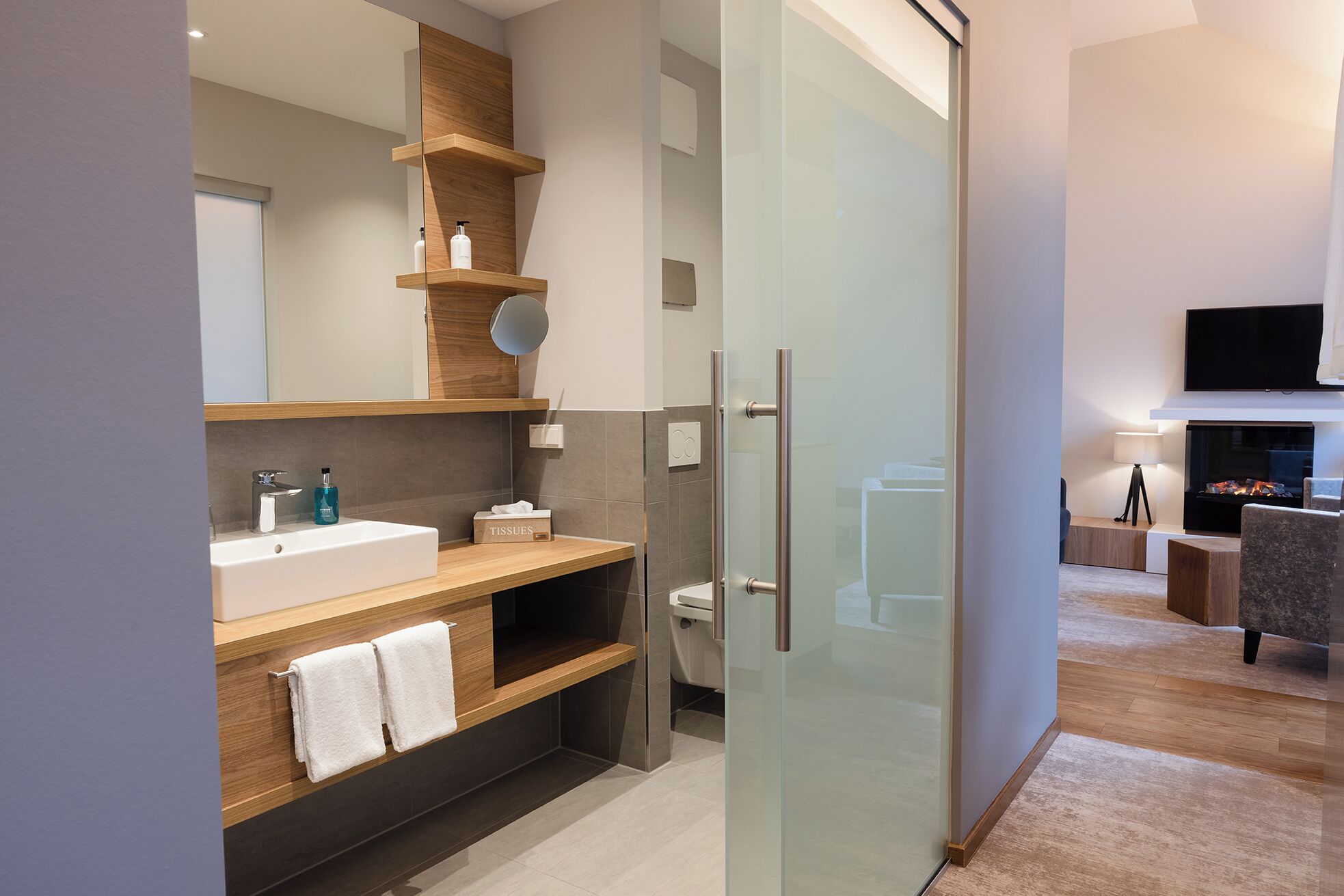 A modern bathroom with a glass shower enclosure, wooden vanity, and a large mirror.