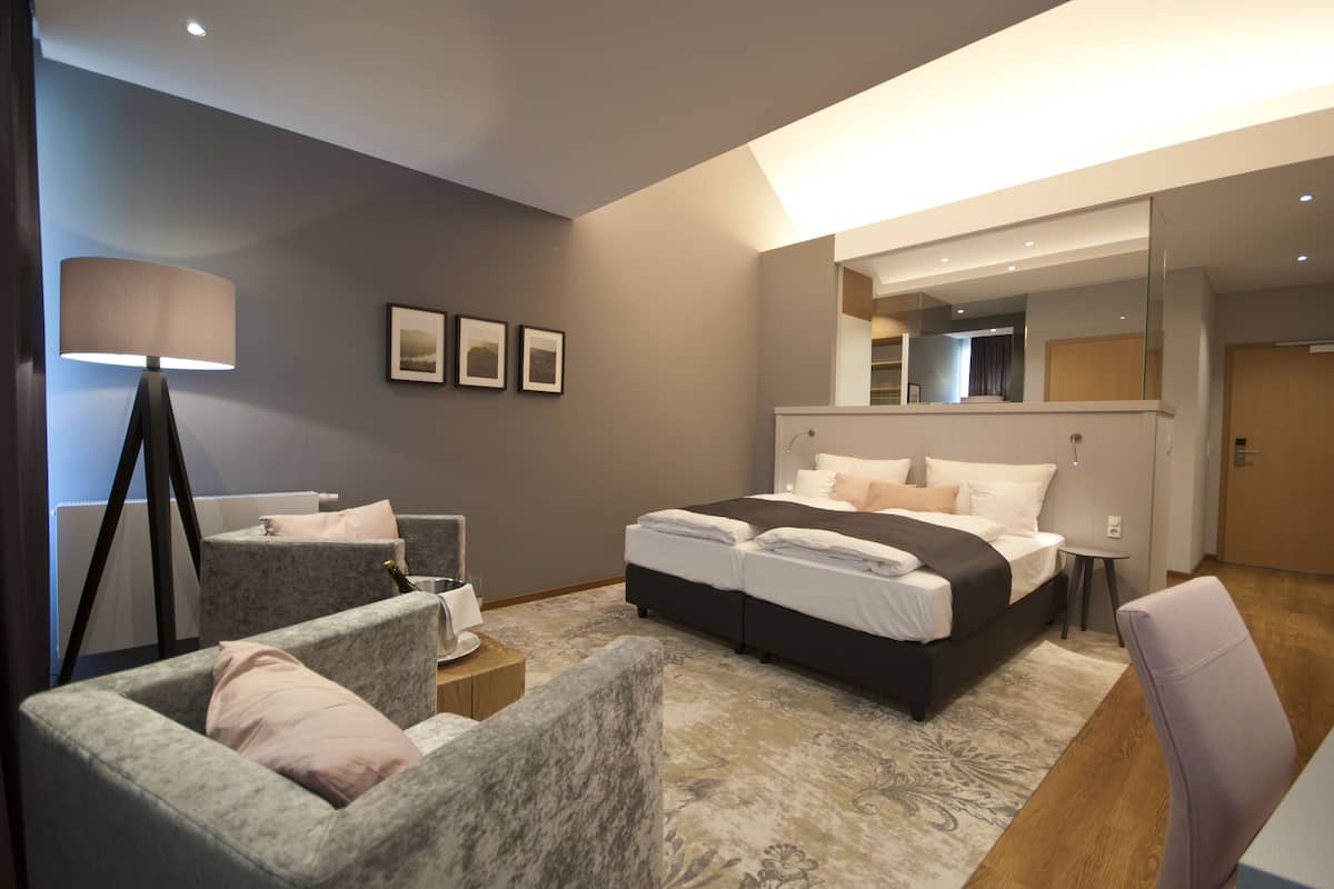 A modern hotel room with a large bed, two armchairs, a small table, and a floor lamp.