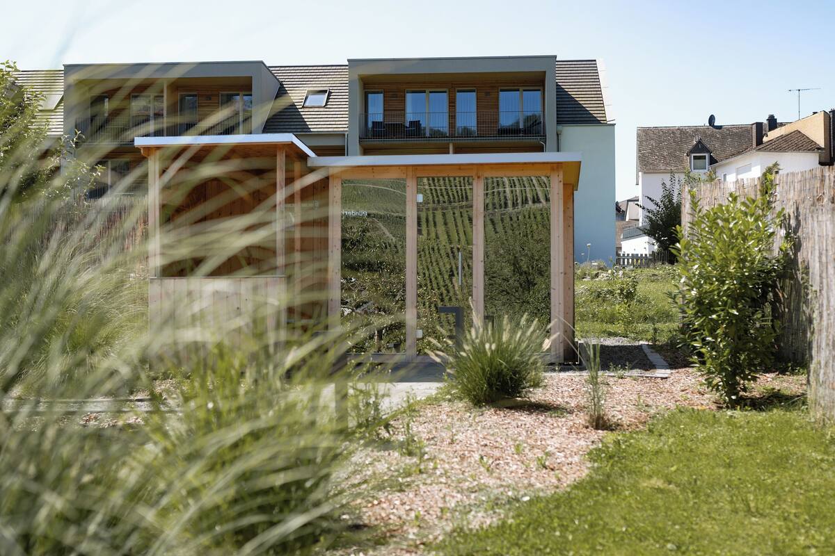 A modern house with a large balcony, a garden with grass and shrubs, and a clear sky.