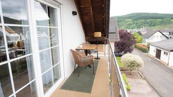 A balcony with a table and chairs, a small rug, and a view of a residential street and hills.