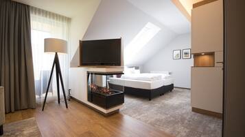 A modern hotel room with a large bed, a flat-screen TV, a fireplace, and a large window with curtains.