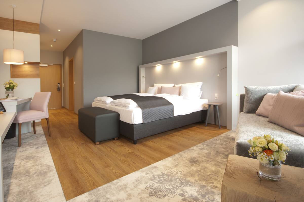 A modern bedroom with a large bed, a desk, a chair, and a sofa.