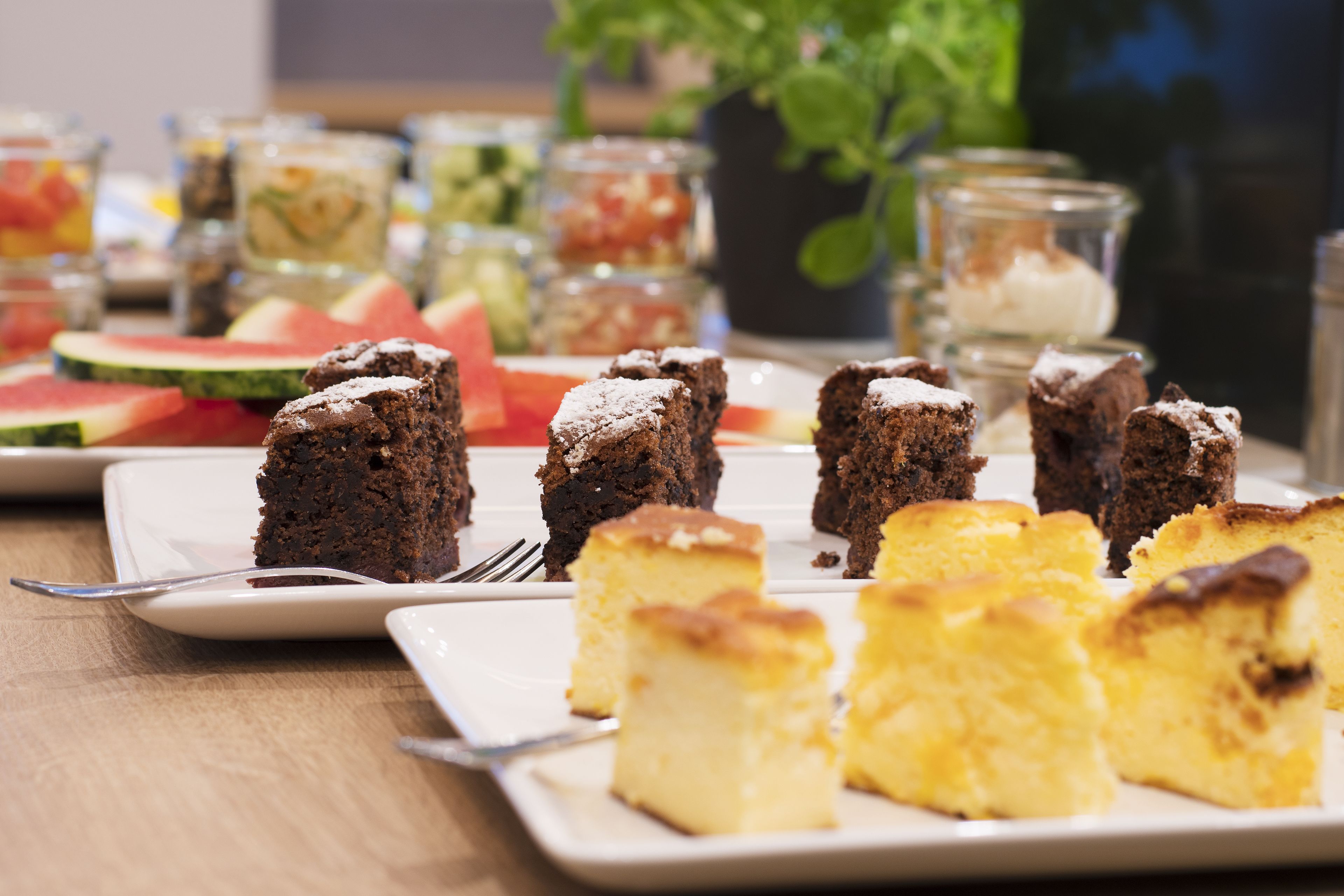 A dessert table with various cakes and a watermelon slice.