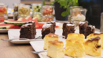 A dessert table with various cakes and a watermelon slice.