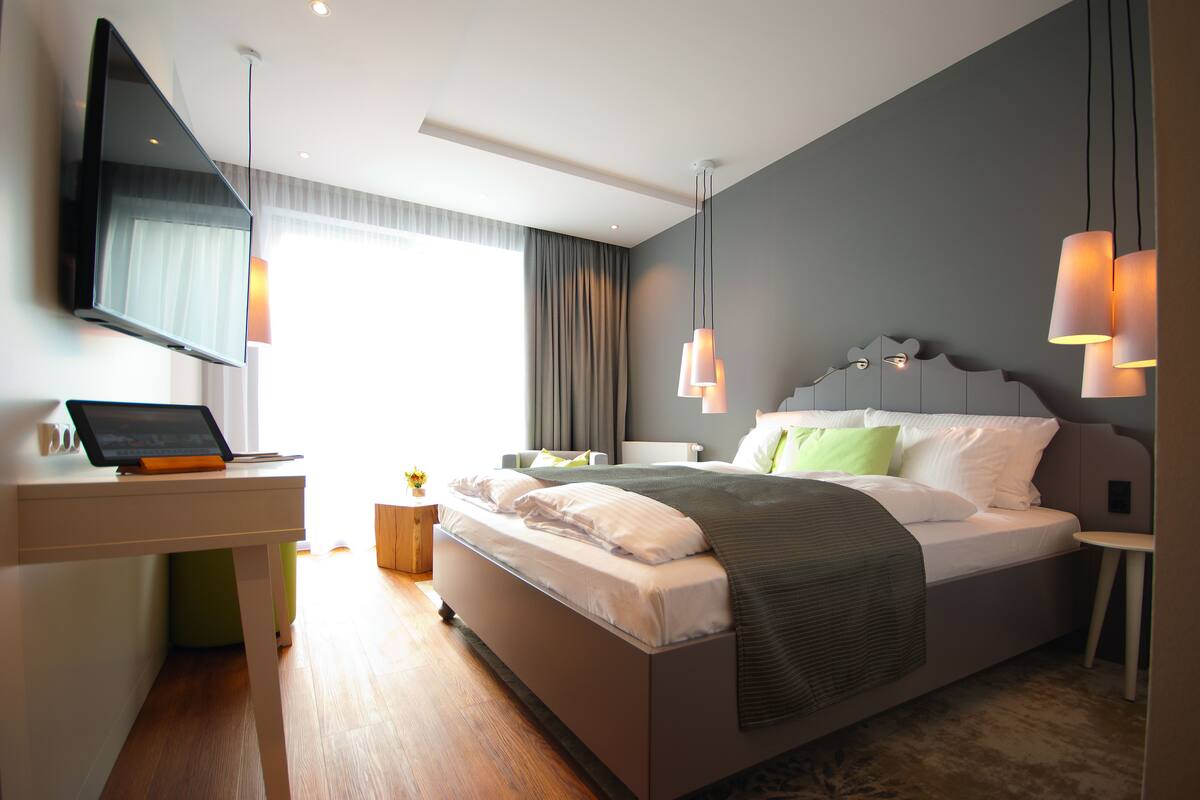 A modern hotel room with a bed, a desk with a laptop, a flat-screen TV, and ambient lighting.