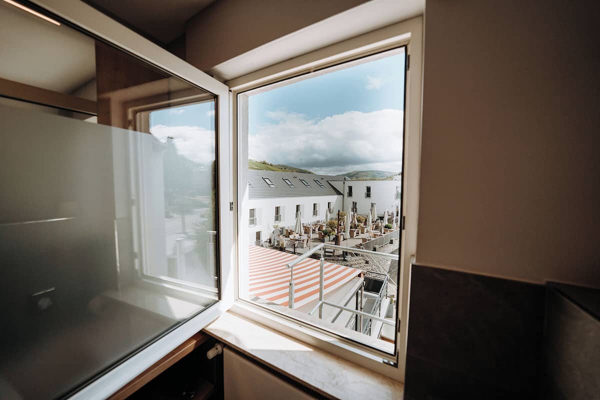 A room with a large window overlooking a courtyard with outdoor seating and a building in the background.
