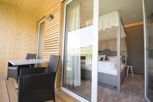 Una habitación con una cama, una mesita y una silla, y vistas a un paisaje verde a través de un ventanal.