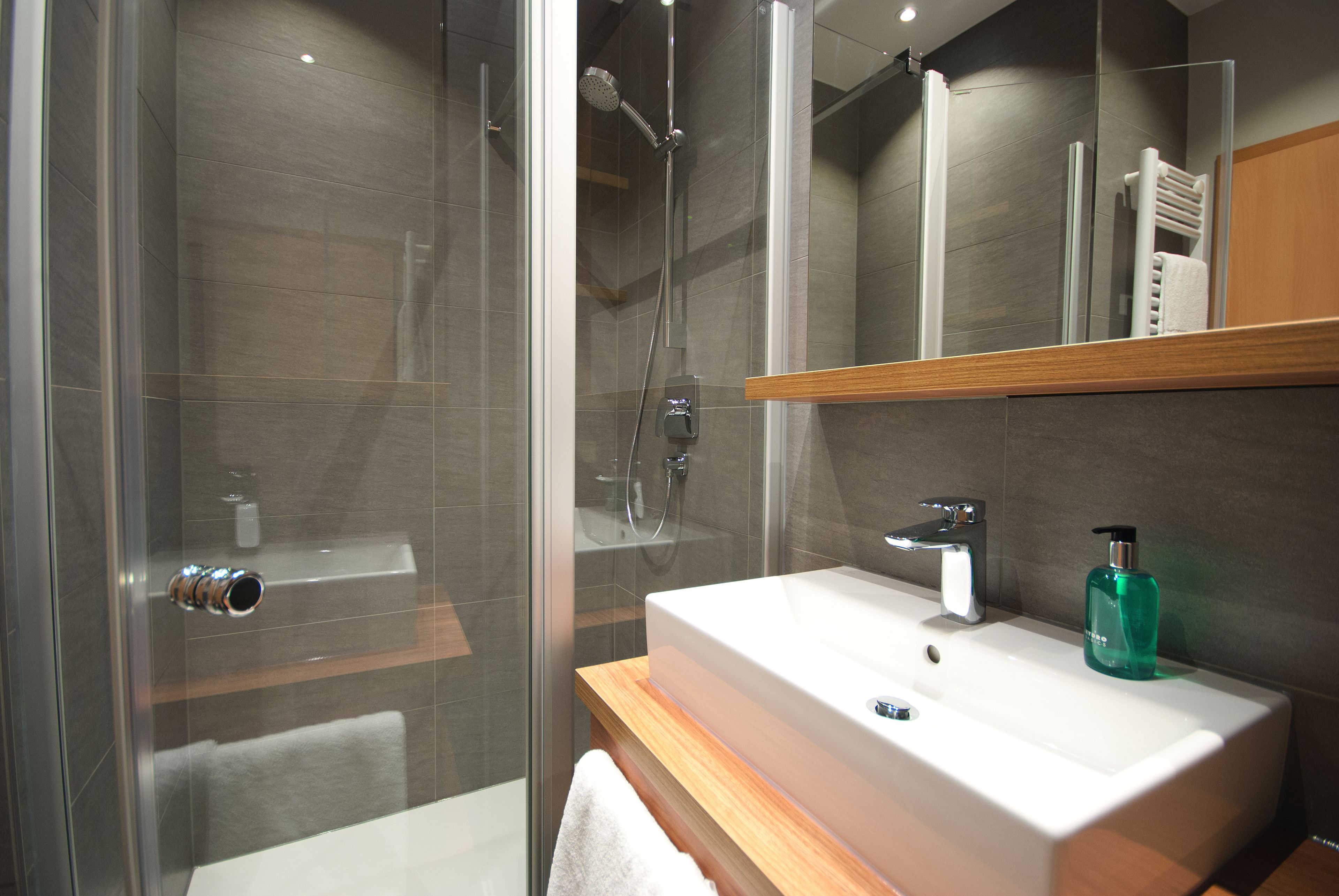 A modern bathroom with a glass-enclosed shower, a white sink, and a wooden vanity.