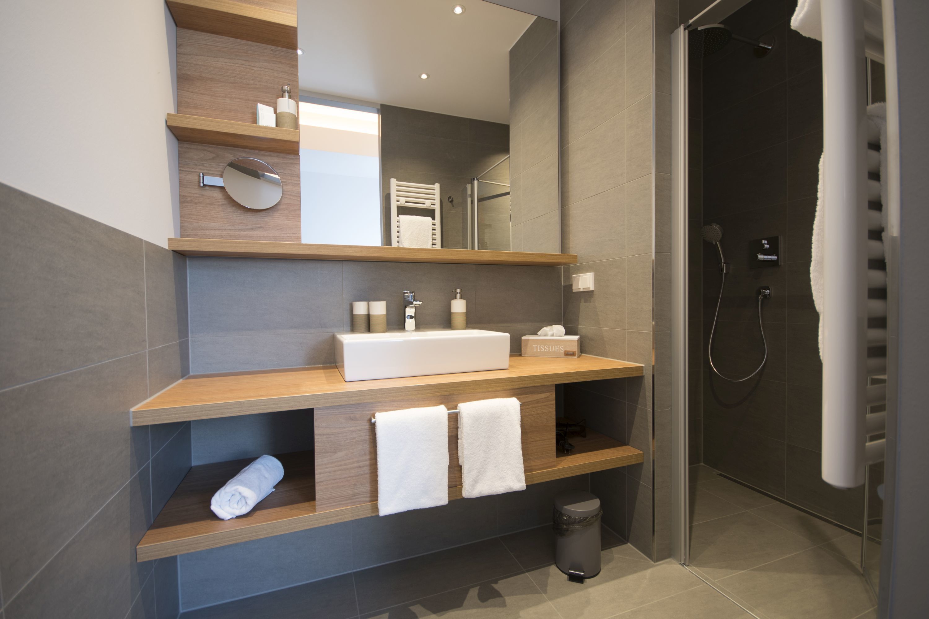 A modern bathroom with a wooden vanity, a large mirror, a built-in sink, and a walk-in shower.
