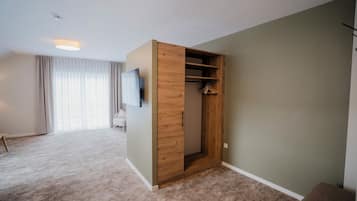 A room with a built-in wooden wardrobe, a flat-screen TV mounted on the wall, and a large window with sheer curtains.