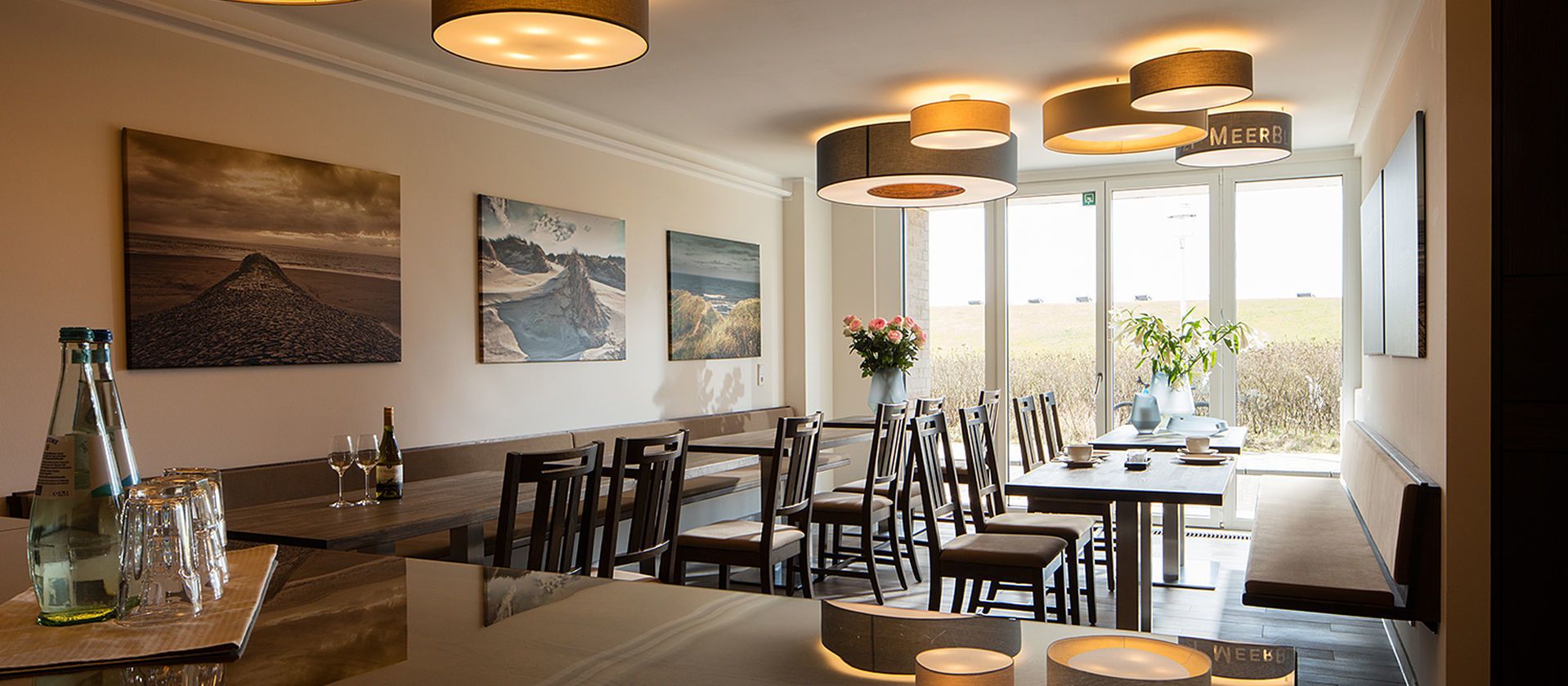 En restaurant med høje borde, stole og hængende pendellamper.