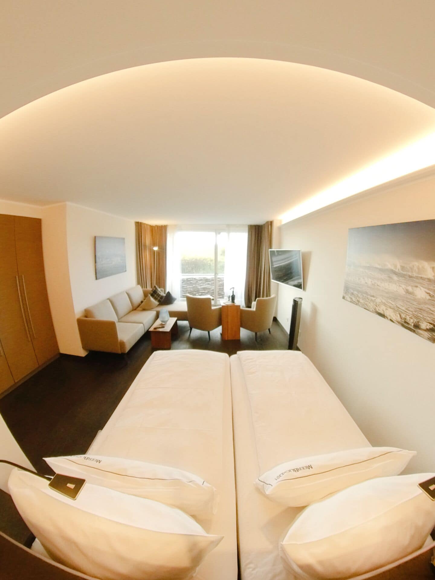 A hotel room with two beds, a sofa, a TV, and a window with curtains.